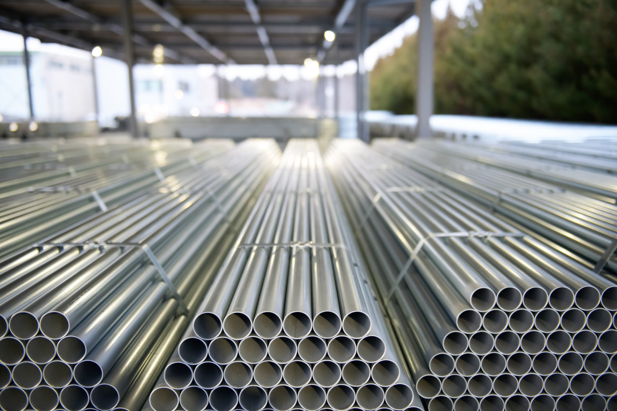 Stacked bundles of high-quality industrial steel pipes and scaffolding tubes inside a manufacturing facility. The circular cross-sections of the galvanized steel pipes are neatly organized in rows, showcasing a uniform, lightweight design. The setting reflects an industrial warehouse environment, emphasizing durability, precision engineering, and the scale of sustainable construction materials ready for global distribution.
