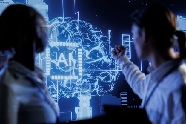 Two engineers brainstorm in front of a digital screen featuring a glowing blue human brain and the letters "AI." The futuristic interface illustrates the concept of a "corporate brain," connecting human insight with artificial intelligence to optimize knowledge sharing and data management.